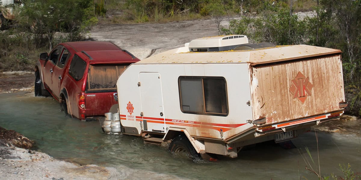 Off-road caravan navigating the rugged Telegraph Track in Queensland, surrounded by lush greenery and rough terrain.