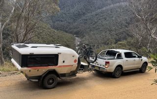 A Kimberley Kube teardrop camper trailer parked on a remote dirt road, surrounded by dry grass and distant trees, highlighting its off road capability.