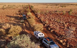 Kruiswagen off-road motorhome and Karavan off-road caravan traveling along a remote Australian desert track, surrounded by vast arid landscapes.