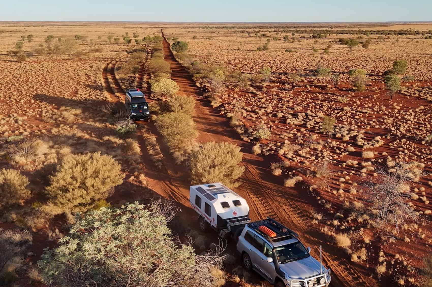 Kruiswagen off-road motorhome and Karavan off-road caravan traveling along a remote Australian desert track, surrounded by vast arid landscapes.
