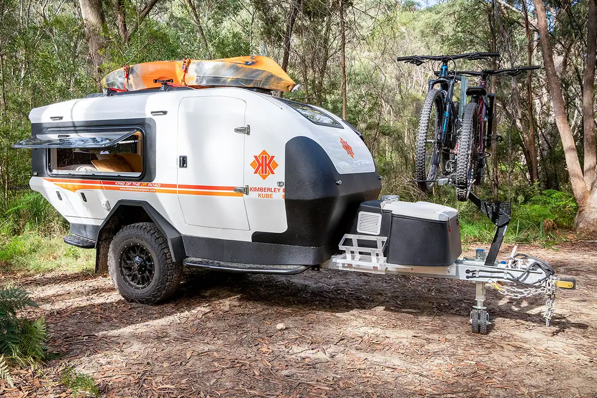 Teardrop camper with iSi bicycle rack attached, parked outdoors with Australian bush background.