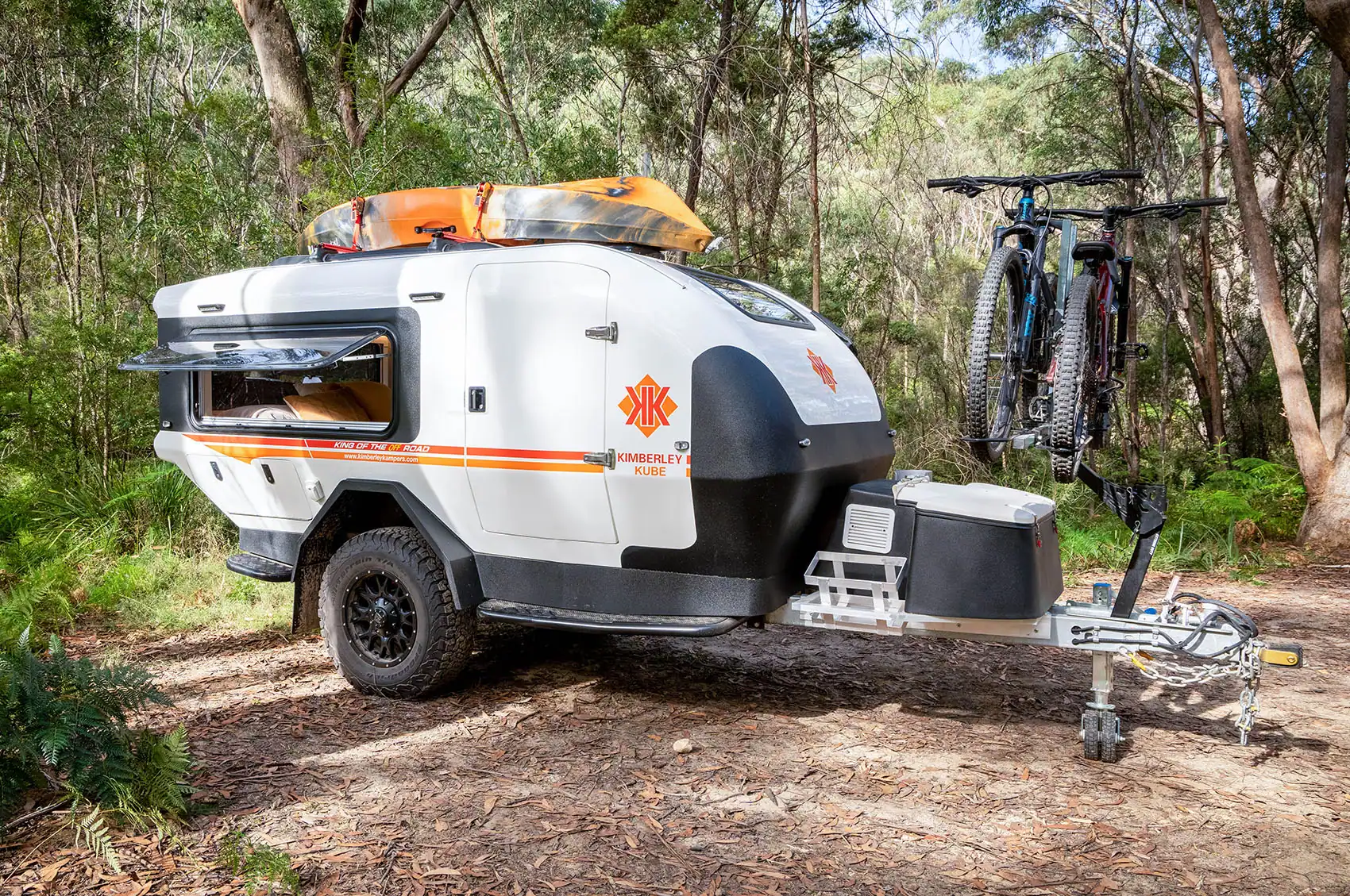 Teardrop camper with iSi bicycle rack attached, parked outdoors with Australian bush background. Passenger side view.