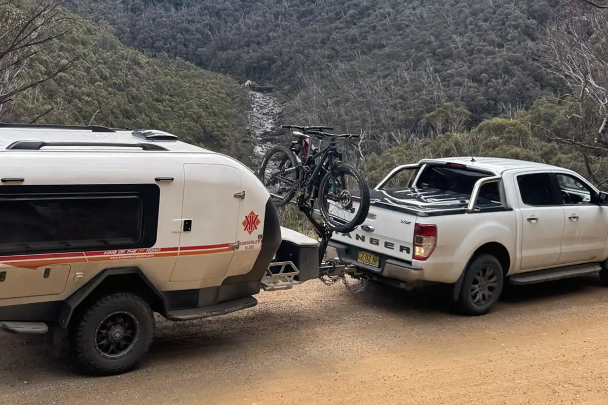 Teardrop camper with iSi bicycle rack attached, parked outdoors with scenic Australian background.