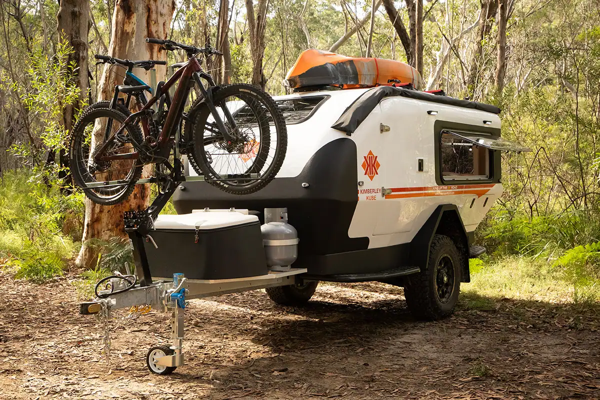 Teardrop camper with iSi bicycle rack attached, parked outdoors with Australian bush background. Passenger side view.