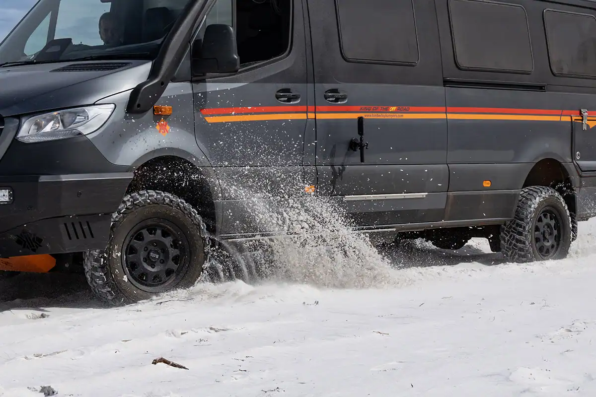 Kimberley Kampers offroad motorhome driving through shallow beach water and wet sand, with dramatic sand spray from the heavy-duty all-terrain tyres, showcasing its beach and coastal off-road capability.